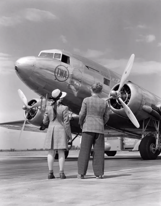 1940S Rear View Of Boy & Girl Standing Together Looking At Propeller Airplane Outdoor