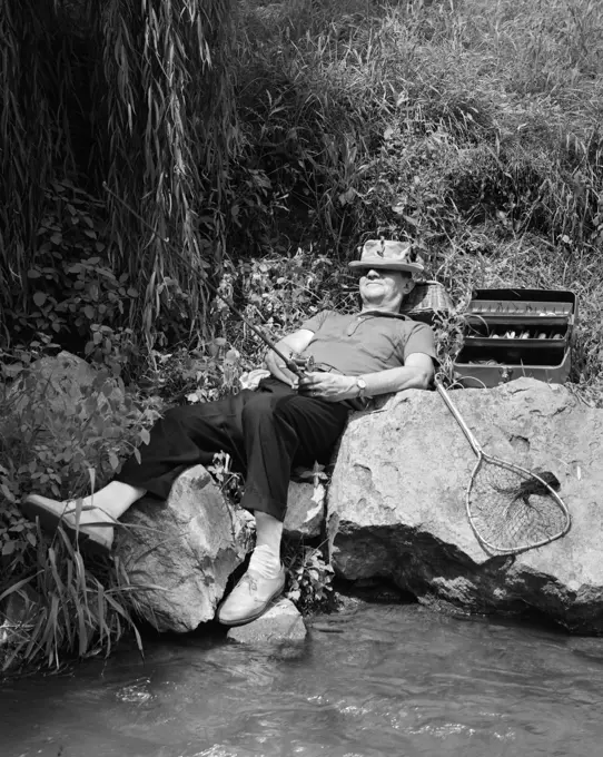 1950S Lazy Fisherman Lying Back On Rock With Hat Pulled Over Eyes Fishing In Creek