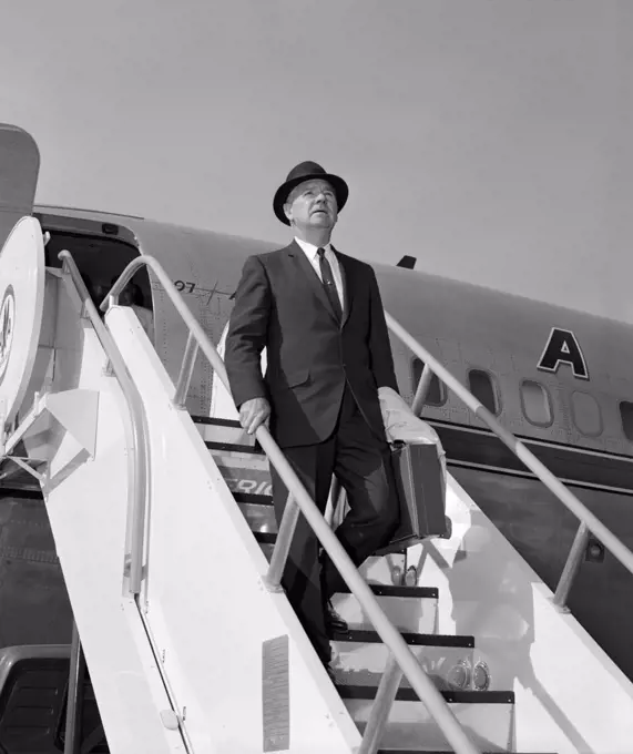 1960S Businessman Deplaning From Airplane Wearing Hat And Carrying Overcoat And Briefcase