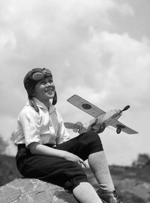 1930S Boy In Leather Aviator Cap With Goggles Sitting On Rock Holding Model Plane