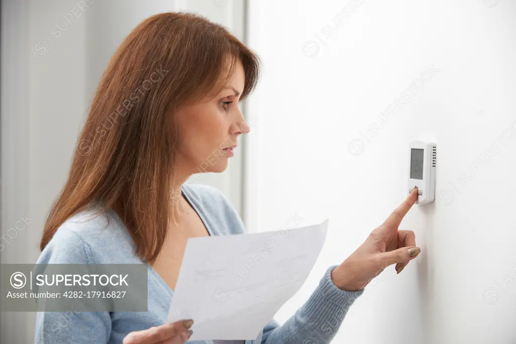 Worried Woman Turning Down Central Heating Thermostat