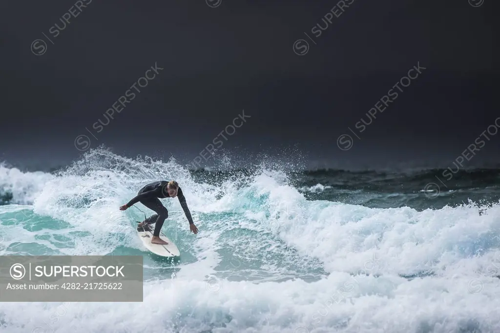 A lone surfer riding a wave as dark clouds gather over the North Cornwall coast.