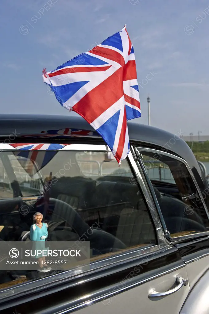 England, Kent, Chatham. A small figure of Queen Elizabeth ll in the window of a classic car and a union flag fixed to the outside.
