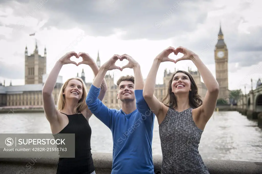 Three friends make a heart shape with their hands with the Houses of Parliament in the background.