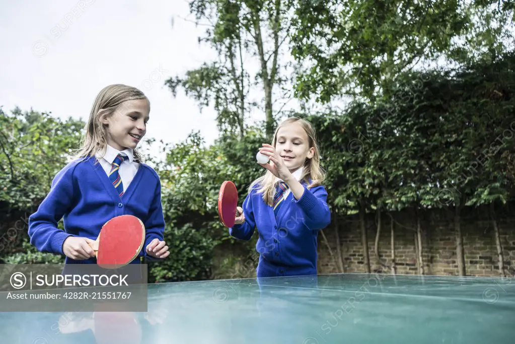 Twin girls in school uniform playing table tennis outside.