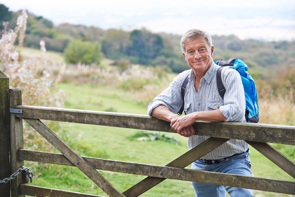 Portrait Of Senior Man On Hike In Countryside Resting By Gate