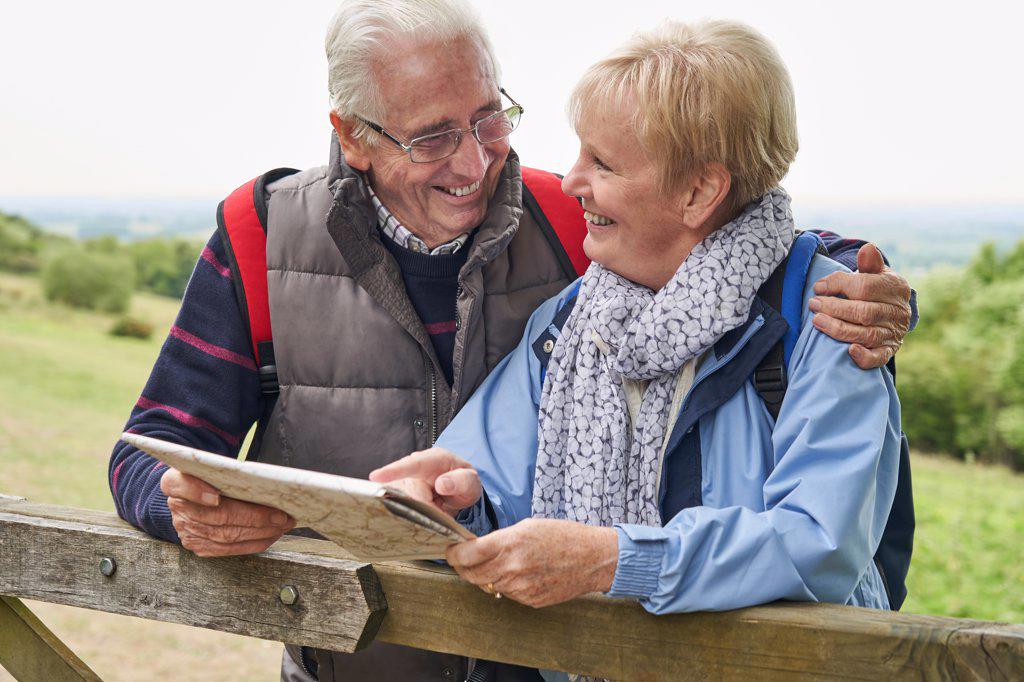 Retired Couple On Walking Holiday Resting On Gate With Map                             