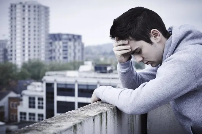 Depressed Young Man Contemplating Suicide On Top Of Tall Building