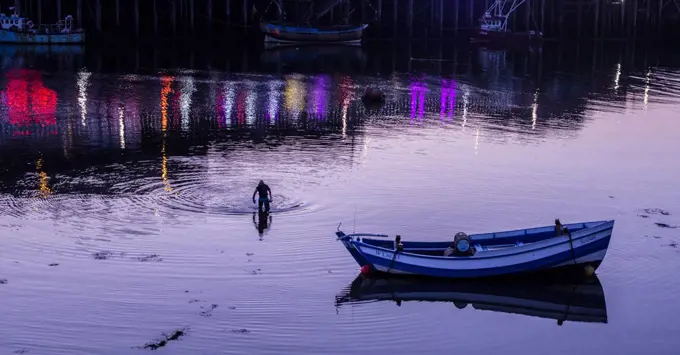 Person in water with boat at dusk in Whitby in England.