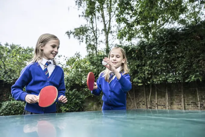 Twin girls in school uniform playing table tennis outside.