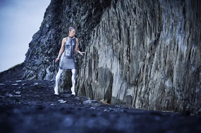 Young women in silver outfit walking with caution into a cave in southern Iceland.