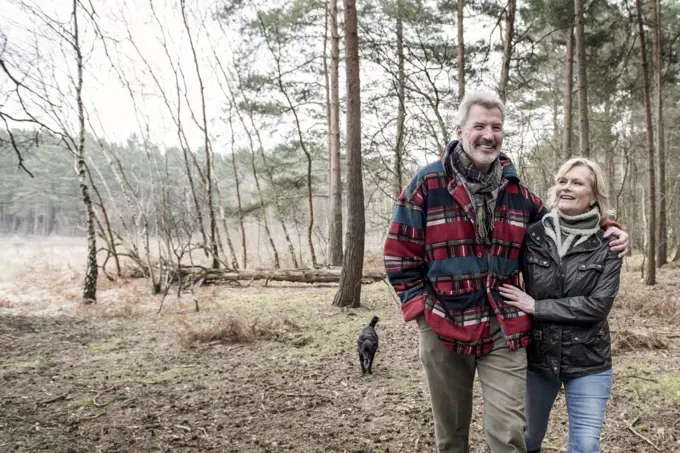 Senior couple enjoying a walk in the woods with their dog.