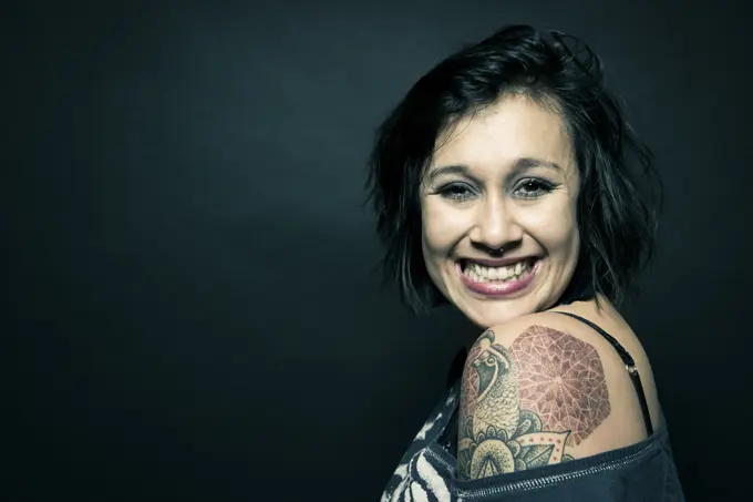 Studio portrait of a woman with a tattoo on her shoulder.