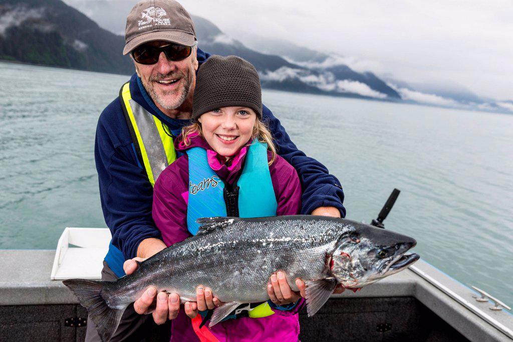 Father and daughter holding up a Silver Salmon while on a boat, Seward, Southcentral Alaska, USA