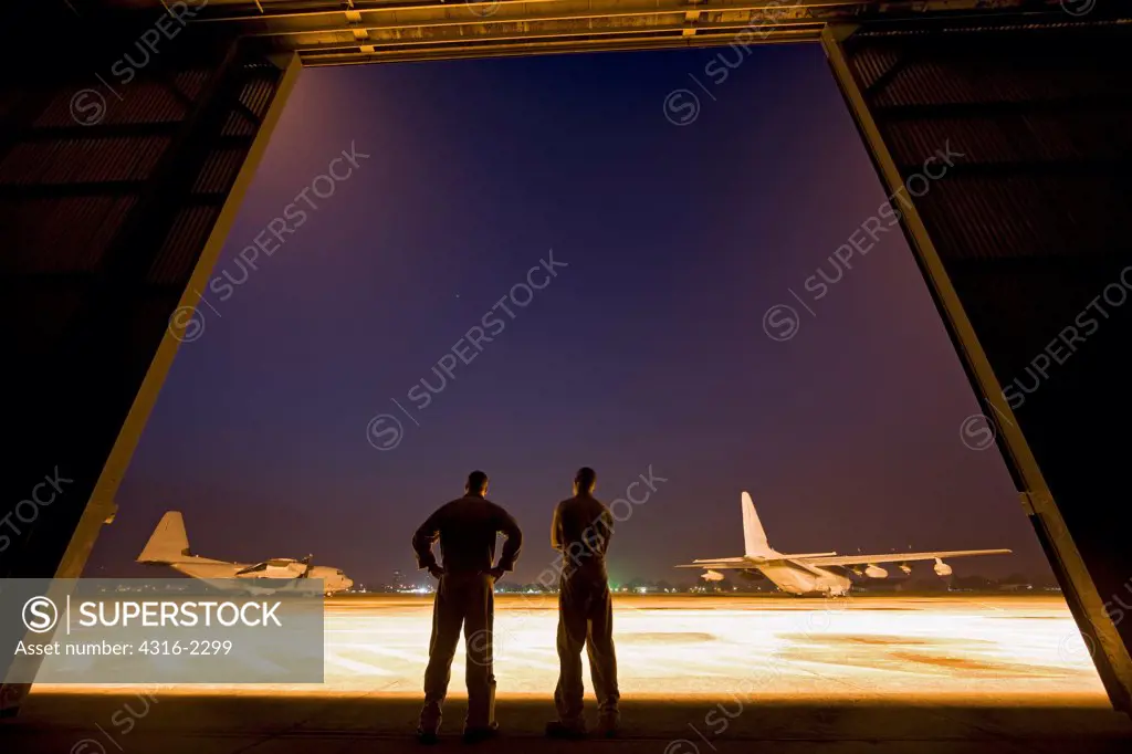 Two United States Marine aviators scan the flight line on which two KC-130J Super Hercules sit parked at Kuantan Air Base, Malaysia.