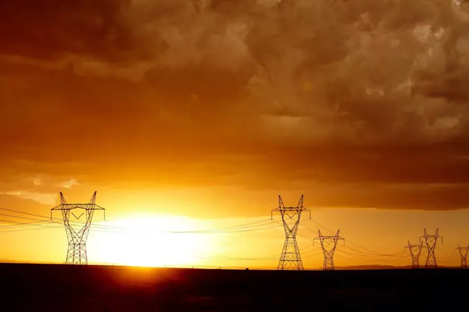 High voltage power lines and transmission towers silhouetted by the setting sun after the passage of a powerful thunderstorm, Colorado