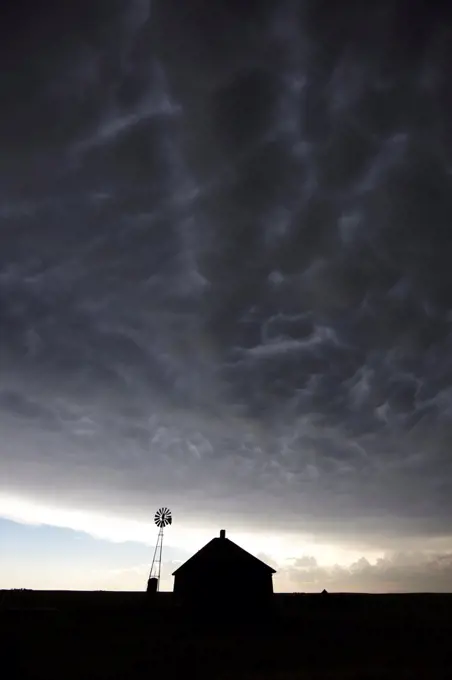 Abandoned ranch house and windmill under a powerful thunderstorm with mammatus clouds, Colorado