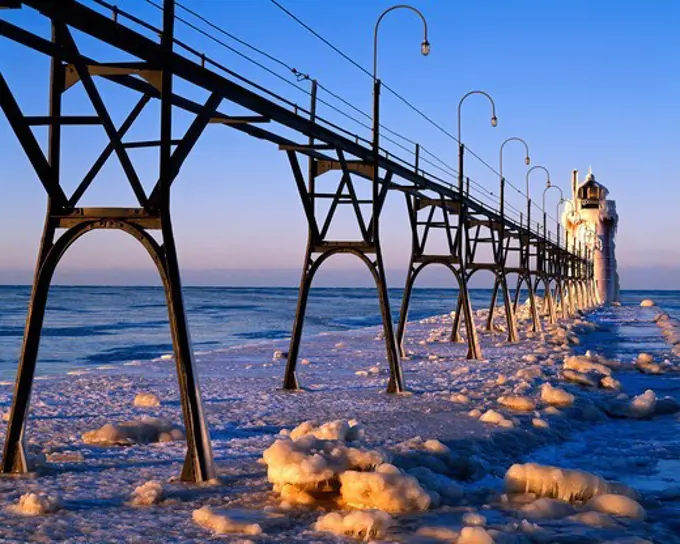 Sunrise light illuminating ice-covered jetty and catwalk leading to the South Haven South Pier Lighthouse, Black River, Lake Michigan, Michigan.