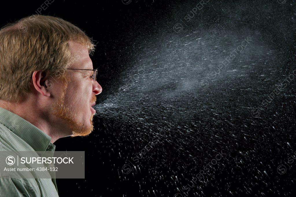 Stock Photo: 4384-132 A sneeze in progress, revealing the plume of salivary droplets as they are expelled in a large cone-shaped array from this man?s open mouth, dramatically illustrating the reason one needs to cover his/her mouth when coughing, or sneezing, in order to protect others from germ exposure. Illnesses like the flu (influenza) and colds are caused by viruses that infect the nose, throat, and lungs. The flu and colds usually spread from person to person when an infected person coughs or sneezes. Photo by