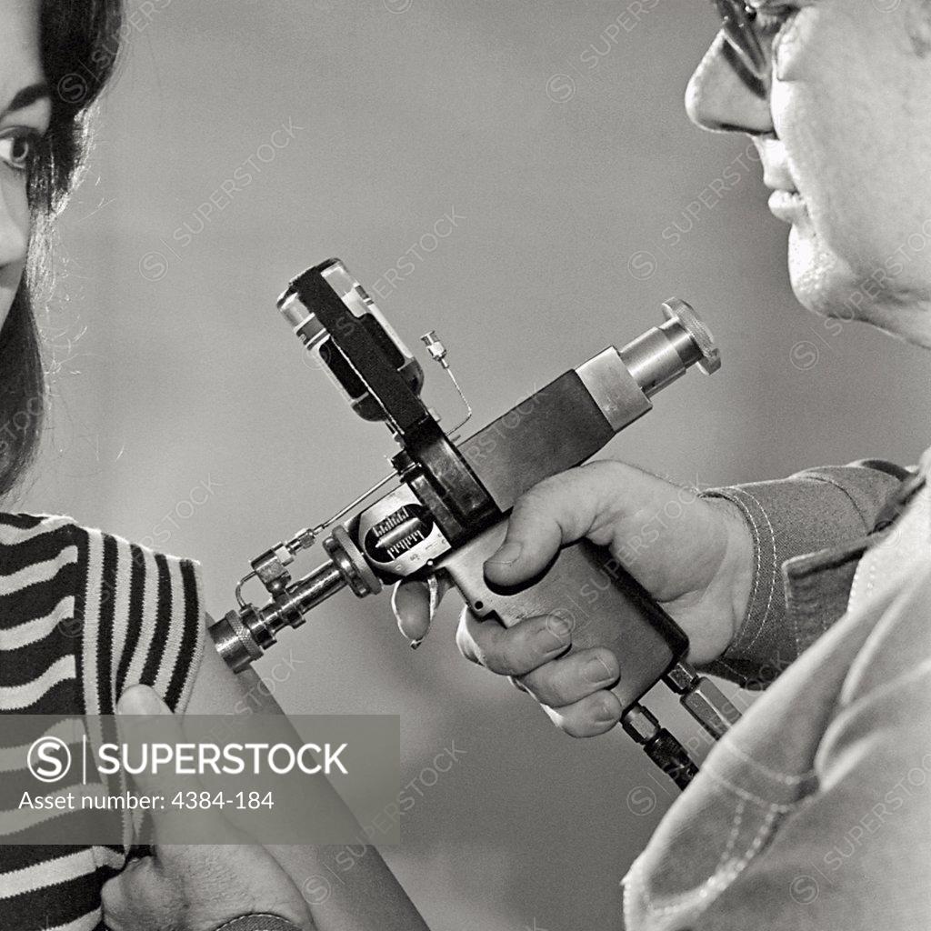 Stock Photo: 4384-184 A man uses a jet injector to innoculate a woman during an immunization project for A/New Jersey/76 influenza.