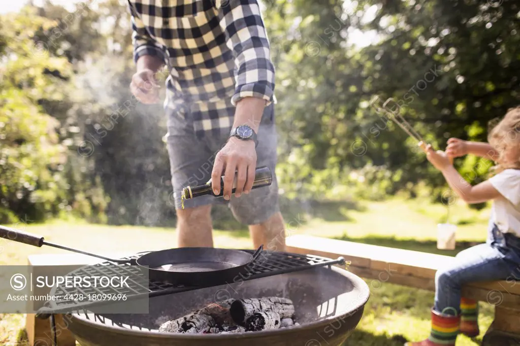 Man pouring olive oil onto cast iron skillet on backyard grill