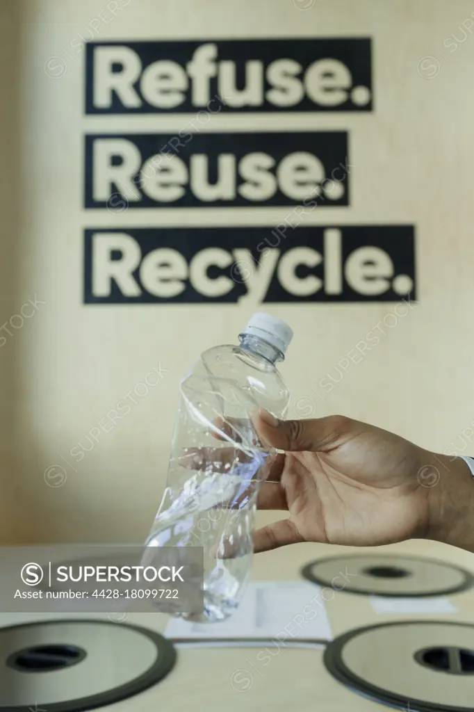 Hand recycling plastic bottle in bin below recycling sign