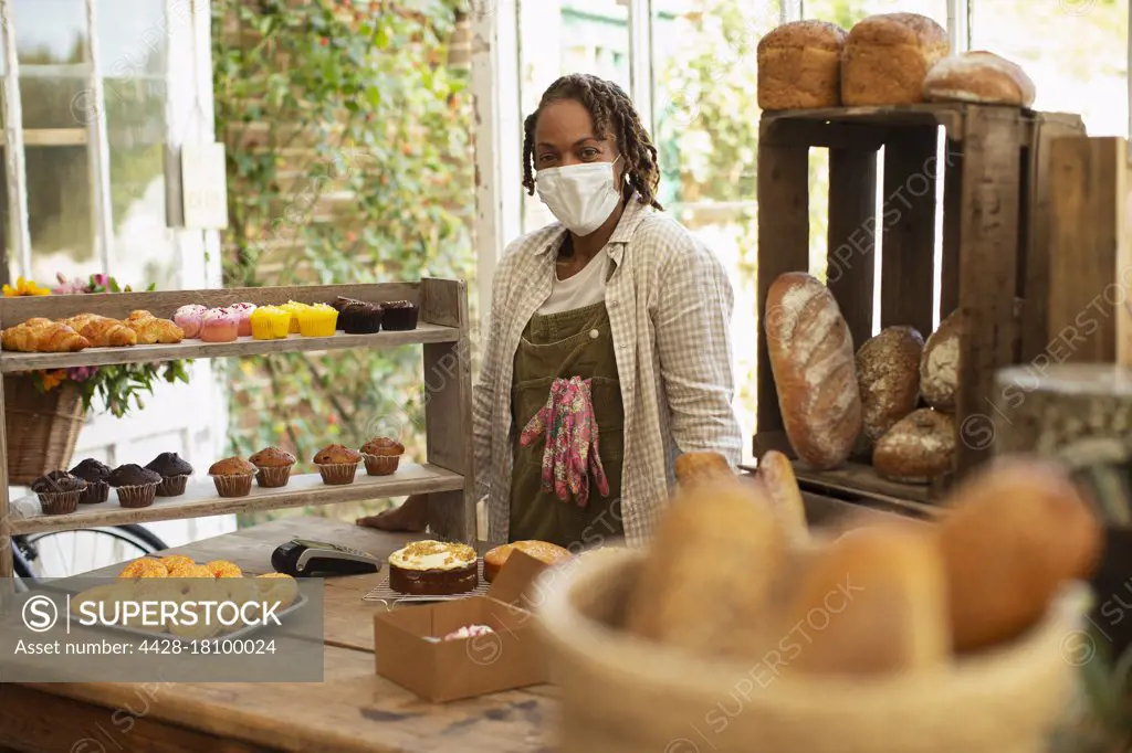 Portrait confident female baker in face mask at pastry display