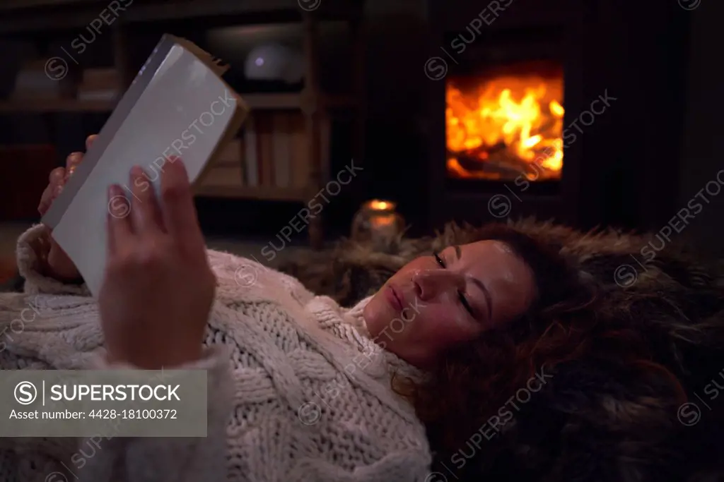 Woman relaxing reading book on blanket at cozy fireside