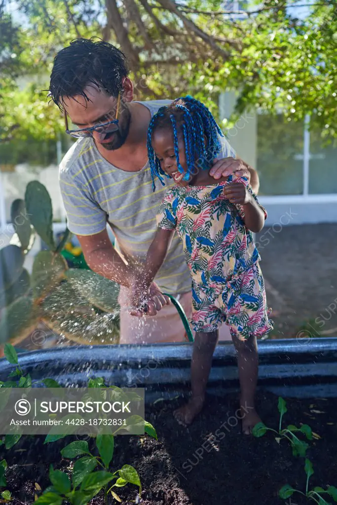Father and toddler daughter watering plants in garden