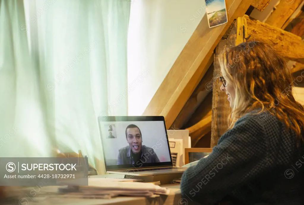 Woman video conferencing with colleague on laptop screen at home