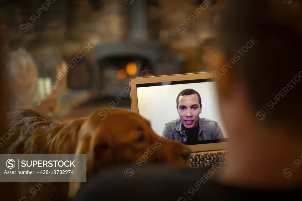 Man with dog video chatting with colleague on laptop screen