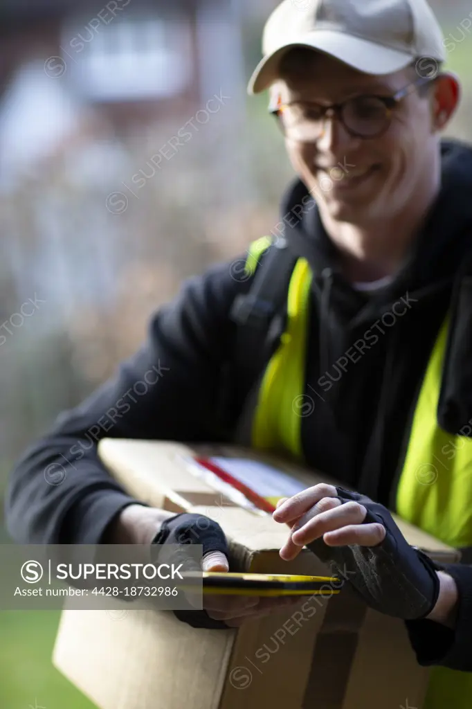 Smiling male courier with smart phone delivering package