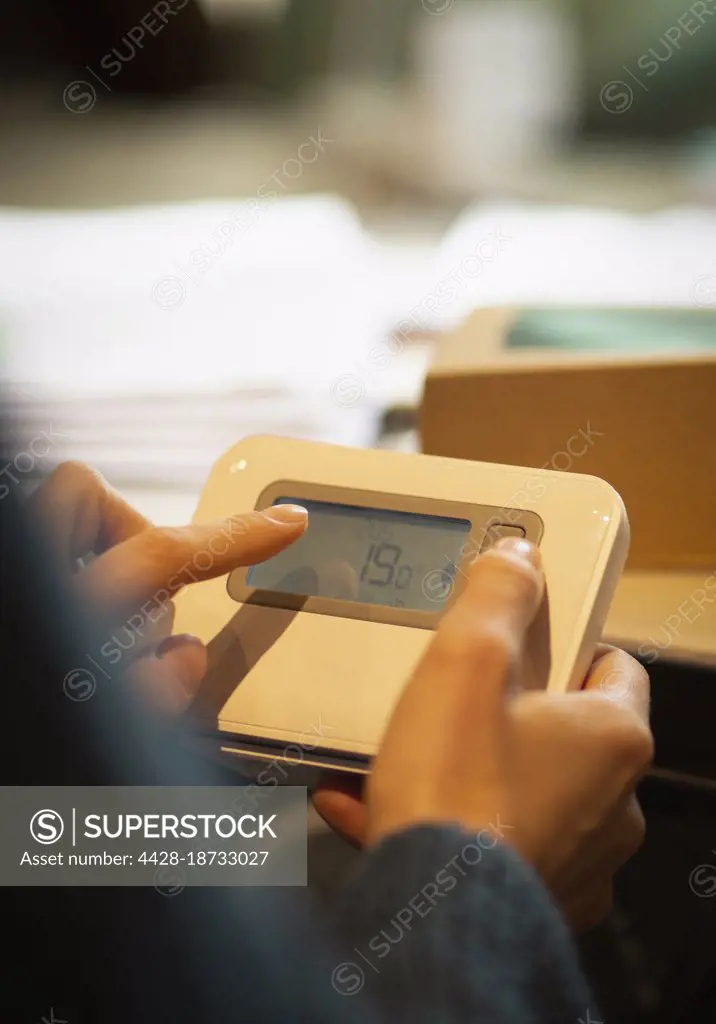 Woman adjusting digital home thermostat