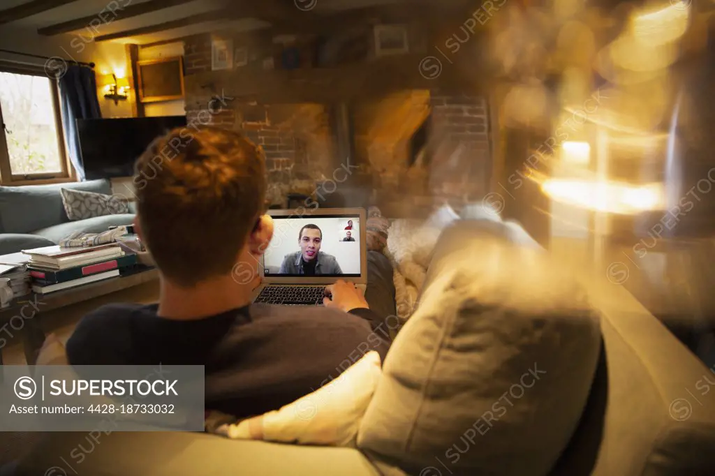 Man video conferencing with colleagues on laptop on sofa