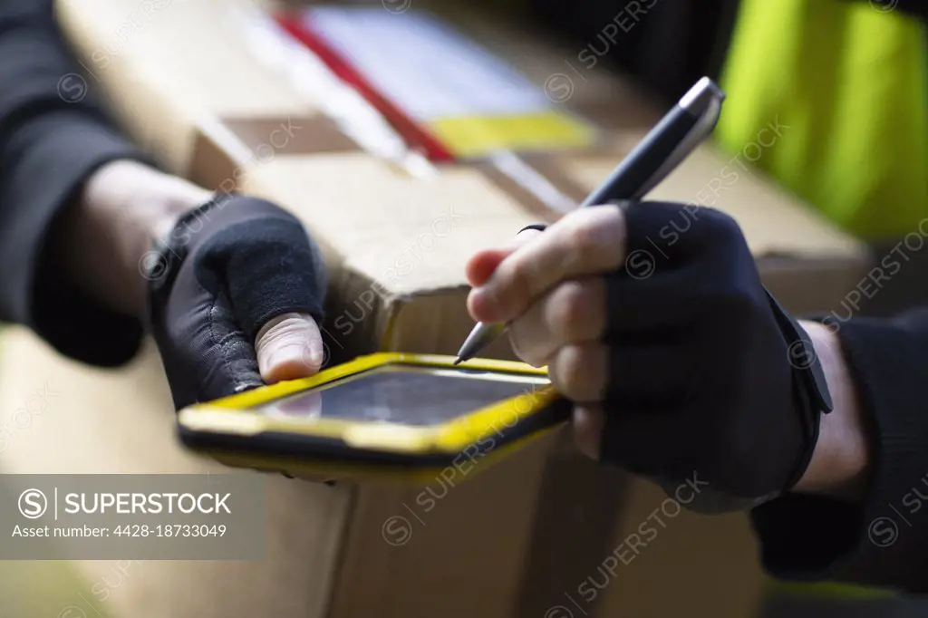 Close up courier with smart phone and stylus delivering package