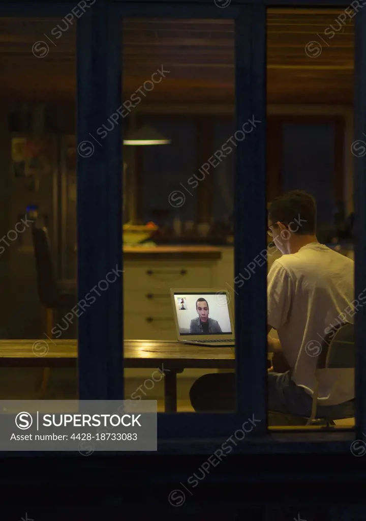 Man working late video conferencing with colleagues in dark kitchen