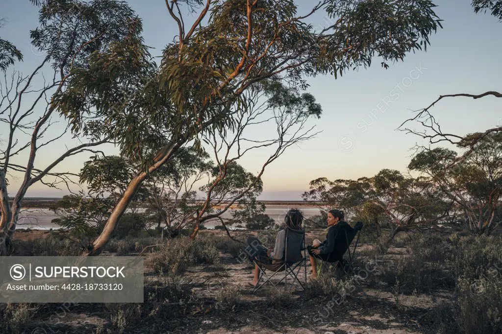 Couple relaxing in camping chairs among trees, Australia
