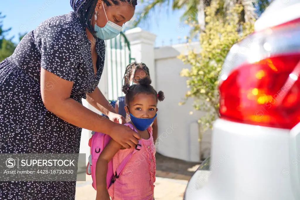 Portrait mother helping daughter in face mask with backpack