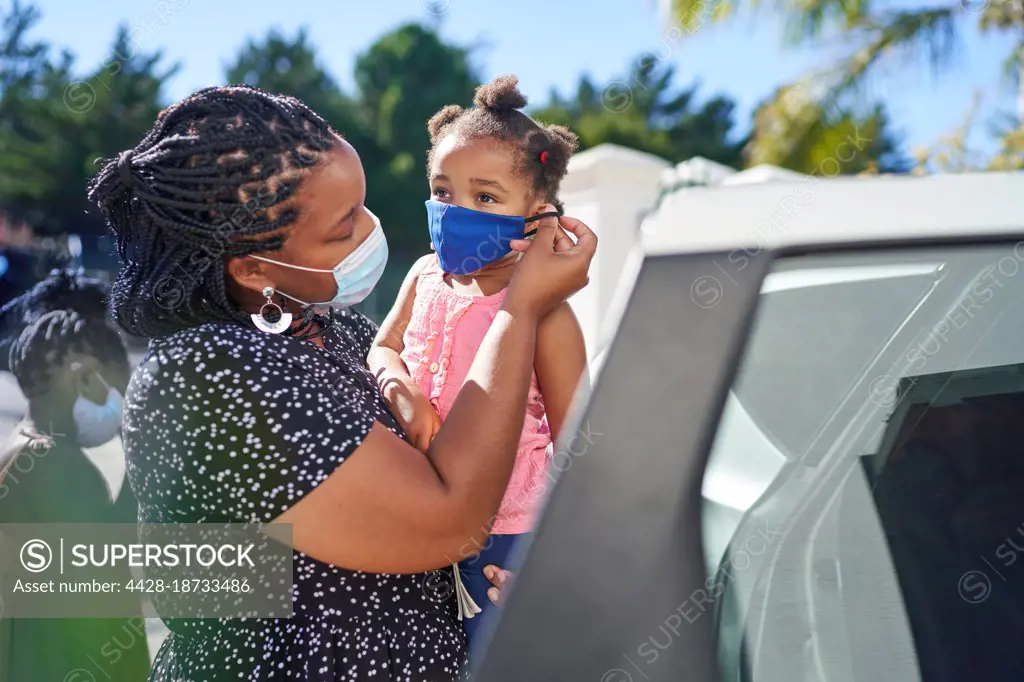 Mother helping daughter with face mask outside car