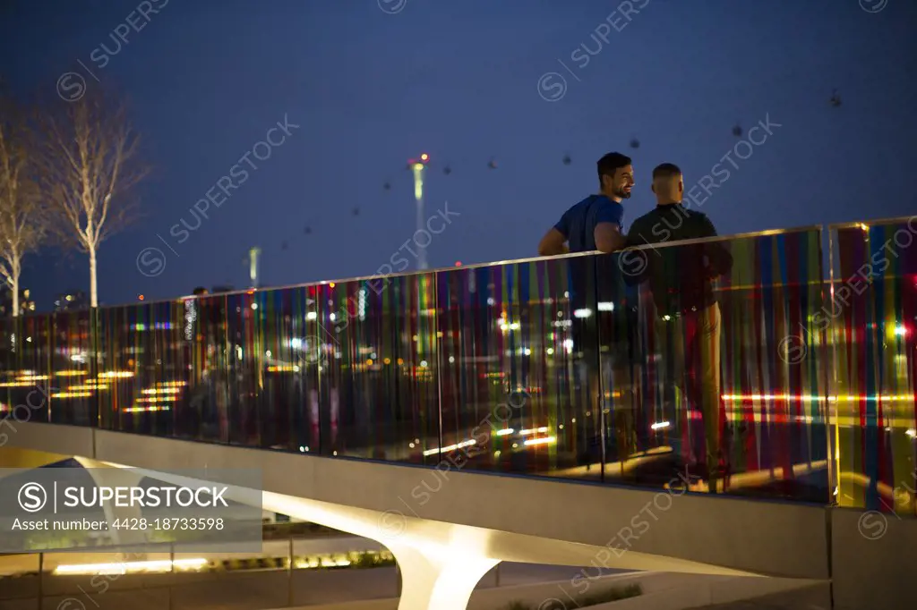 Men talking on illuminated urban footbridge at night, London, UK