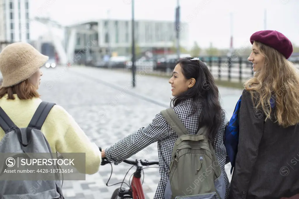 Young women friends with bicycle on urban sidewalk