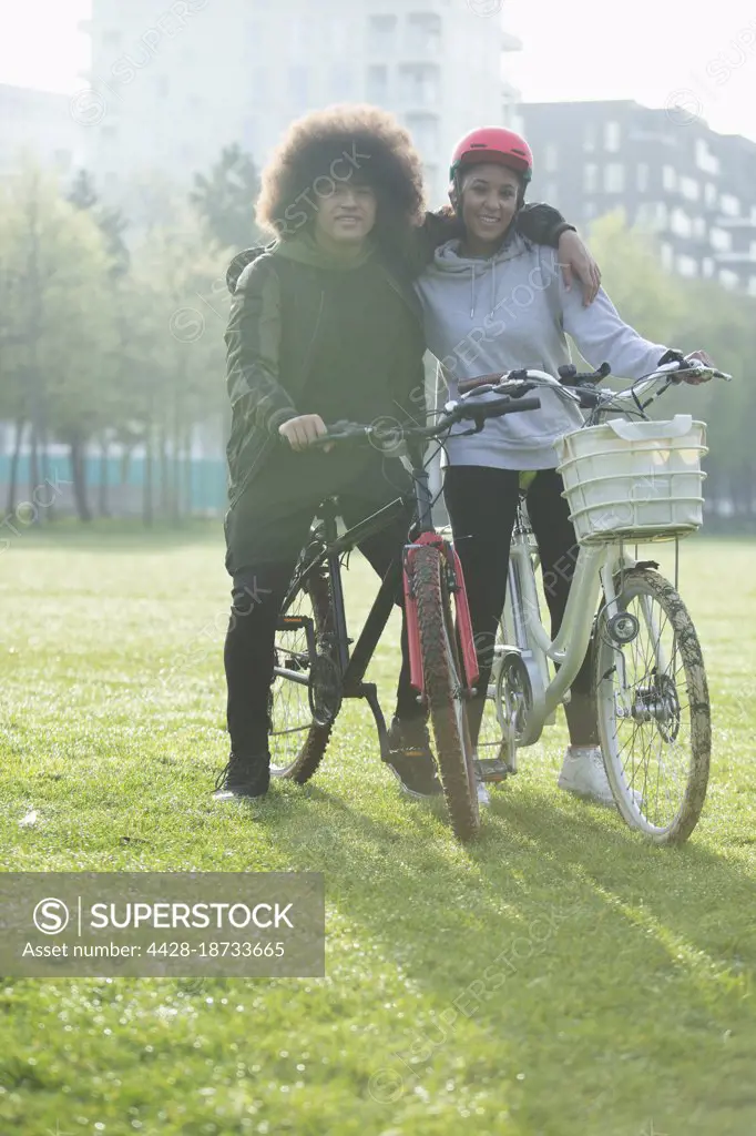 Portrait happy teen couple on bicycles in urban park grass