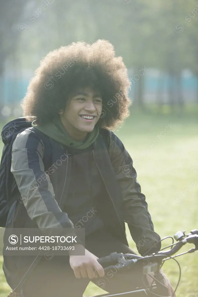 Happy young man with afro on bicycle in park