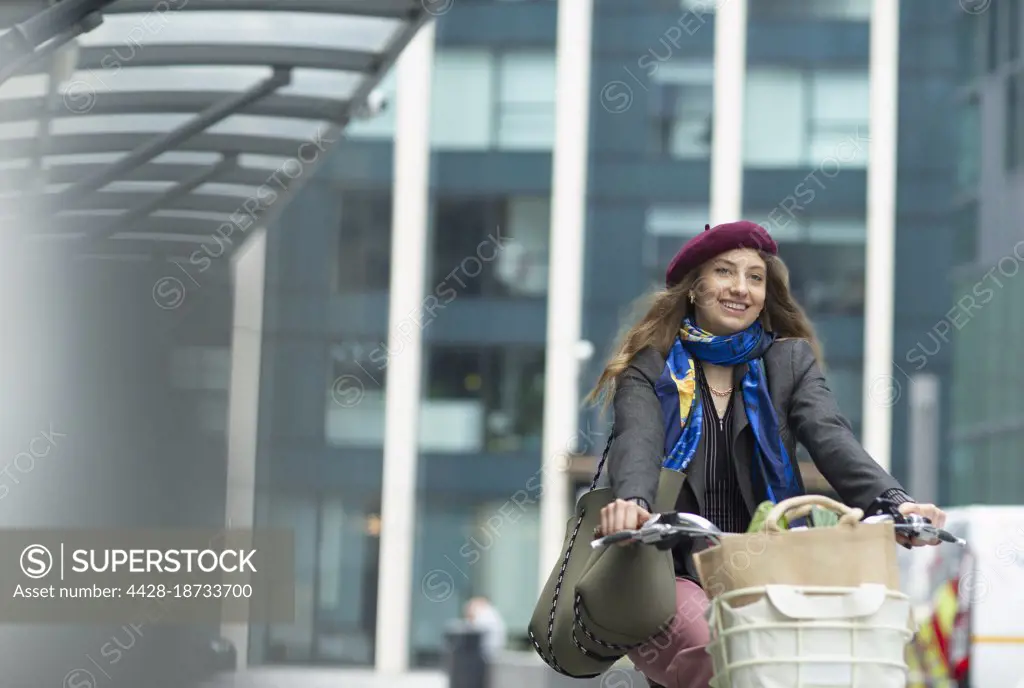 Portrait happy young woman riding bicycle with groceries in city
