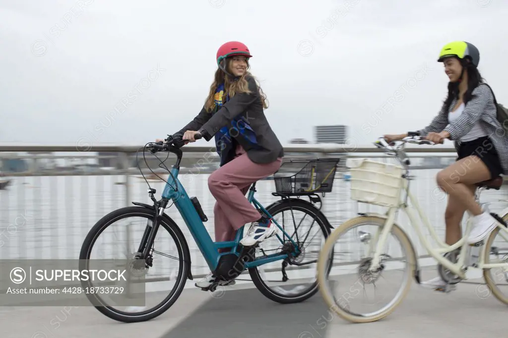 Young women friends riding bicycles on urban bridge