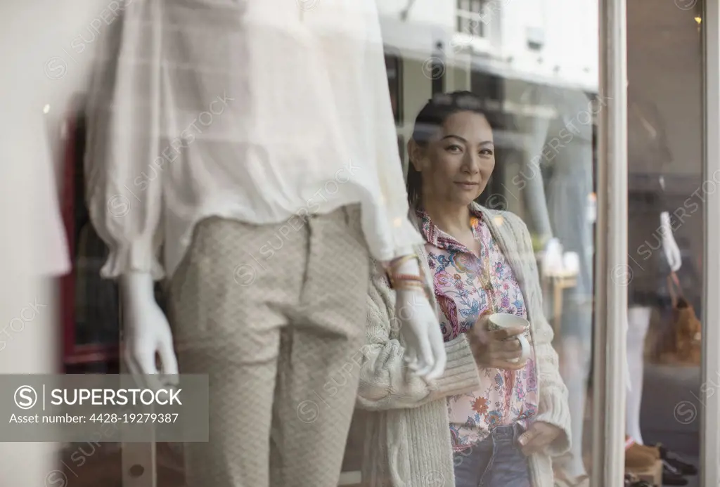 Portrait confident female shop owner drinking tea at boutique window