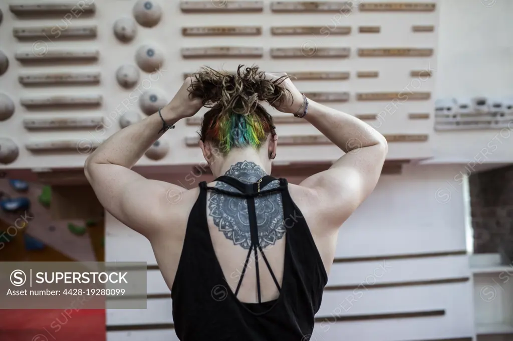 Young woman with mandala back tattoo at rock climbing wall