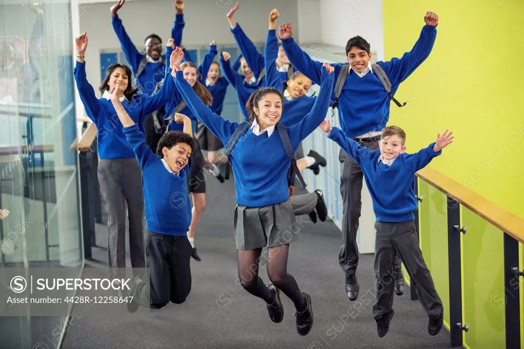 Enthusiastic high school students wearing school uniforms smiling and jumping in school corridor