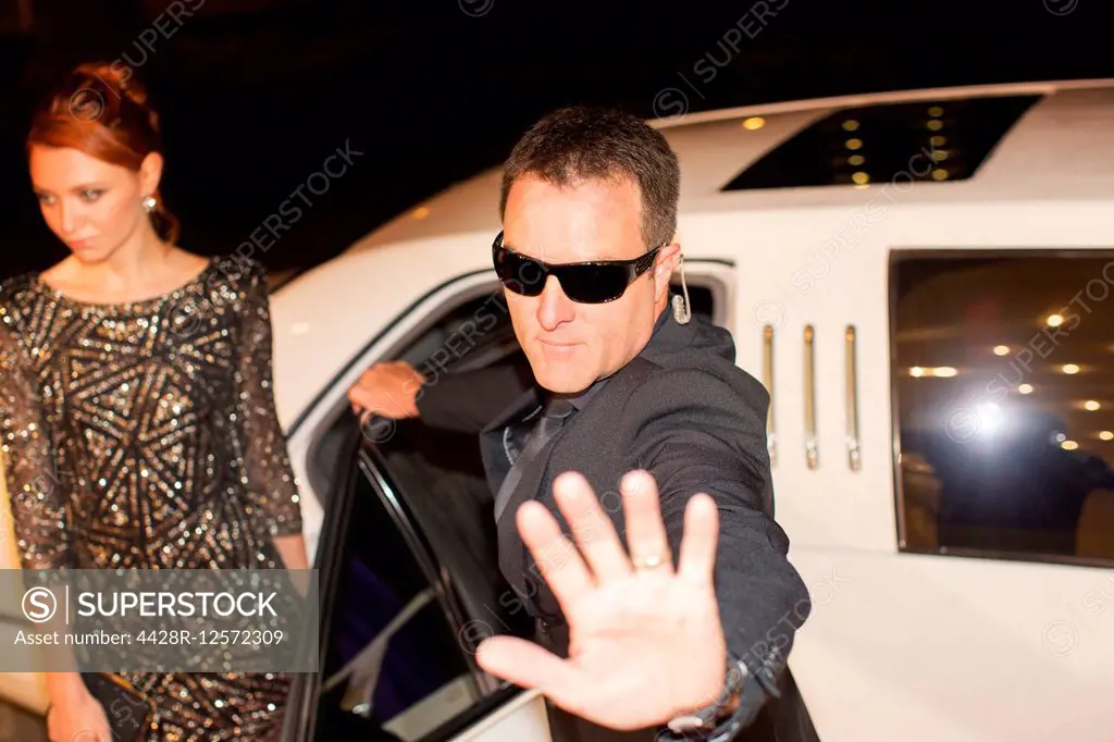 Bodyguard protecting celebrity from paparazzi outside limousine at event
