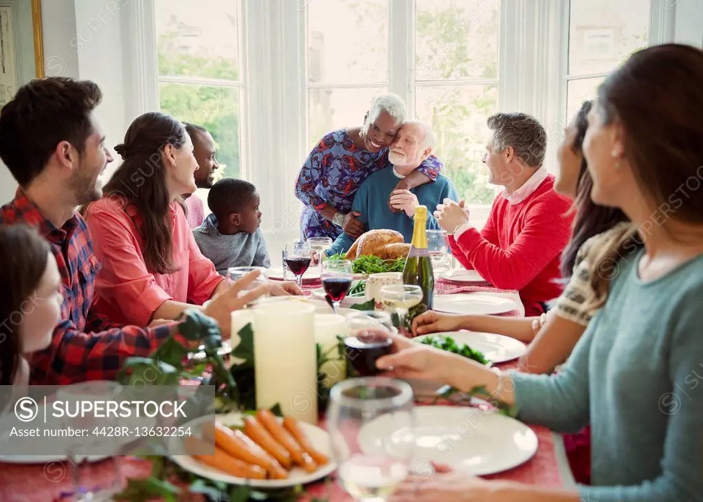 Affectionate multi-ethnic senior couple hugging at family Christmas dinner table